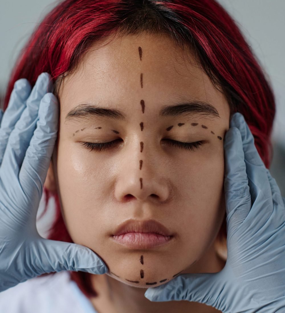 Gloved hands of plastic surgeon touching face of teenage patient with liftmarks while preparing girl for cosmetic procedure